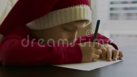 小男孩穿着红色的毛衣戴着一顶红色的圣诞帽手里拿着一支笔头上戴着白色的柚子视频的预览图
