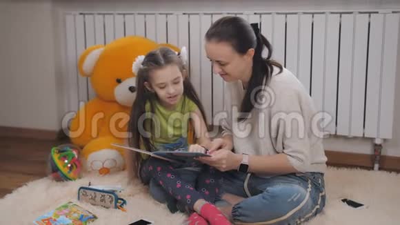 母亲为女儿感到骄傲因为她正在他们公寓的地毯上读一本书视频的预览图