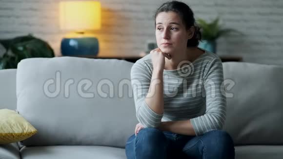 沮丧的年轻女人在家里坐在沙发上思考她的问题视频的预览图
