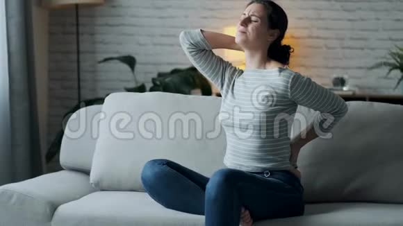 家里客厅里坐在沙发上腰酸背痛的年轻女子视频的预览图