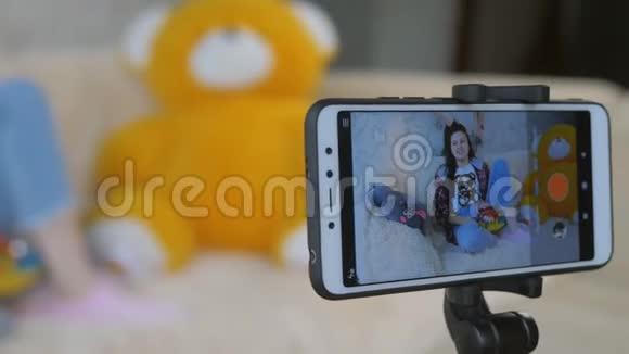 一个十几岁的女孩在智能手机上拍摄一个视频博客站在她面前的三脚架上视频的预览图