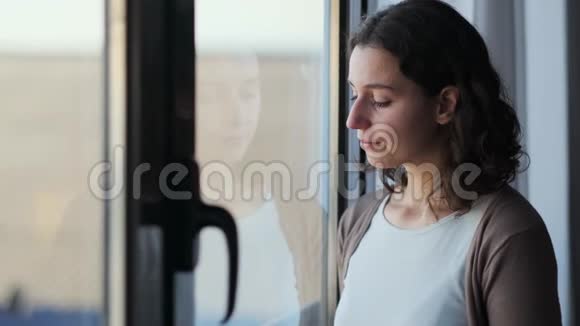 悲伤的年轻女子一边哭一边透过窗户看着家里视频的预览图