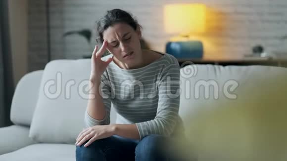 头疼的年轻女人坐在家里客厅的沙发上视频的预览图
