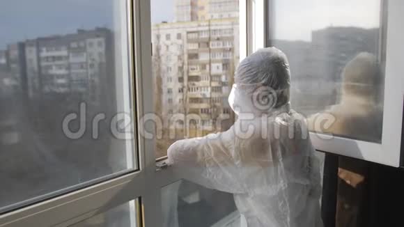 隔离生活穿着防护服的女人和站在窗口的防护面具视频的预览图