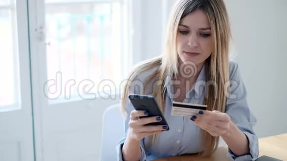漂亮的年轻女人用手机在家里用信用卡在网上购物视频的预览图