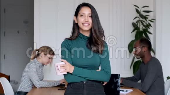 年轻的印度女企业家在办公室里看相机在后台她的同事在工作视频的预览图