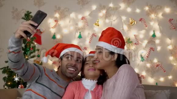 圣诞老人帽子上的快乐印度家庭在圣诞树附近自拍视频的预览图