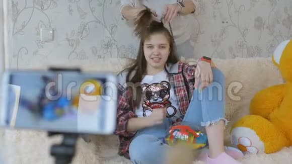这个女孩在一个安装在三脚架上的智能手机前坐在沙发上领导博客的视频博客视频的预览图
