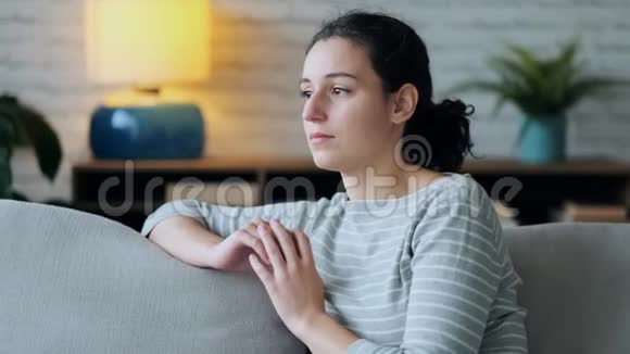 担心的年轻女子一边思考一边坐在家里客厅的沙发上视频的预览图
