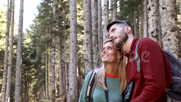 两个徒步旅行者带着背包看风景而女人则指着森林里的东西视频的预览图