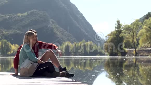 两个徒步旅行者坐着而人指着山上湖中的风景视频的预览图