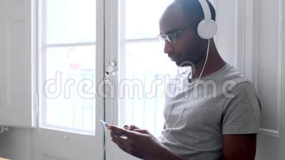 黑人年轻人带着耳机听音乐在家里使用智能手机视频的预览图