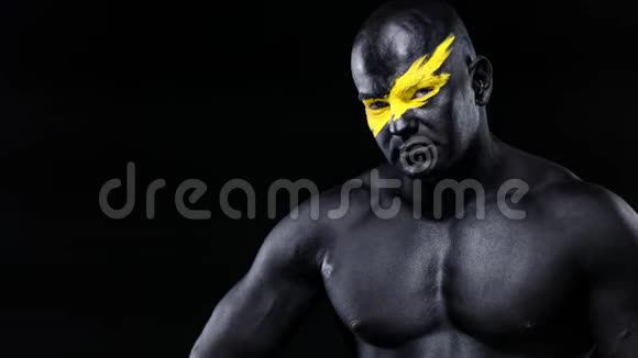 男性健美运动员脸上有黄色的艺术黑色的身体油漆扮演二头肌彩色肖像视频的预览图