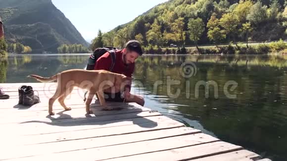 年轻的旅行者徒步旅行者带着背包在湖上给狗送水视频的预览图