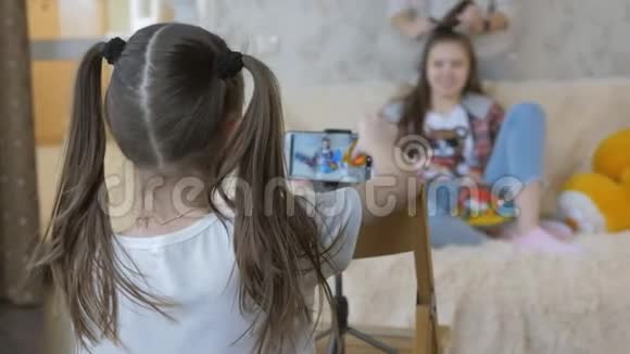这位8岁的女孩在智能手机上拍摄妹妹十几岁的视频坐在沙发上的少女视频的预览图
