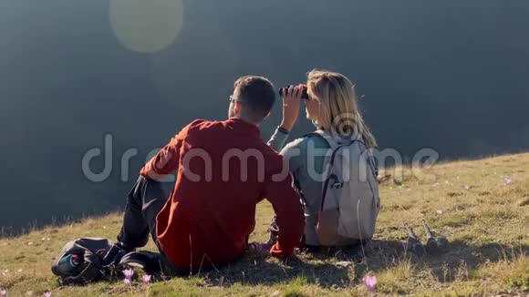 两个徒步旅行者一边欣赏大自然一边用望远镜在山上看风景后景视频的预览图