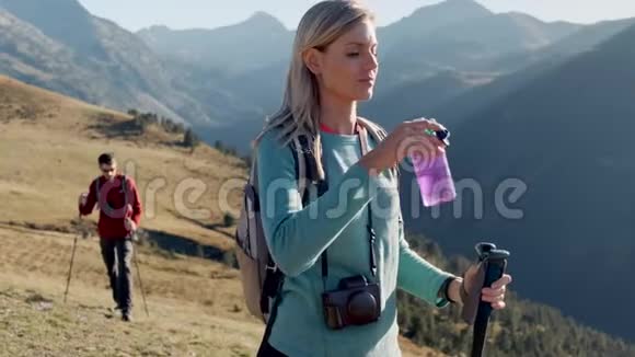 年轻漂亮的女旅行者站在山上背着背包喝水视频的预览图