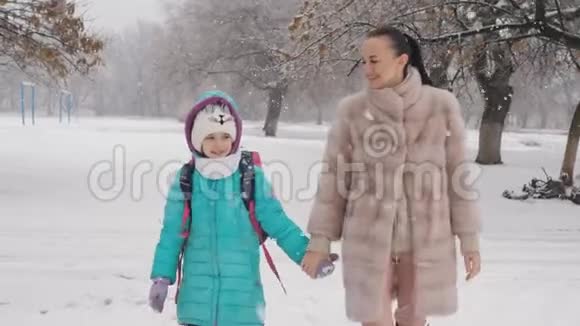 快乐的母亲和她的女儿在冬天在雪地上放学回家视频的预览图