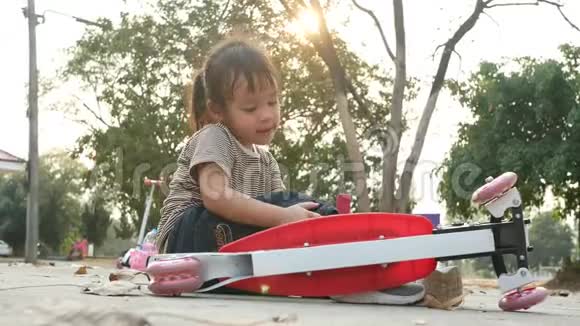 可爱的亚洲小女孩坐在地上后从她的滑板车在夏季公园幼儿健康户外运动视频的预览图