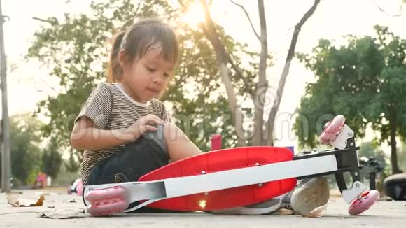 可爱的亚洲小女孩坐在地上后从她的滑板车在夏季公园幼儿健康户外运动视频的预览图