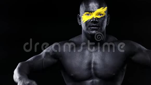 男性健美运动员脸上有黄色的艺术黑色的身体油漆扮演二头肌彩色肖像视频的预览图