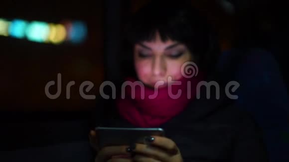 晚上女人在公共汽车的乘客座位上用手中的智能手机视频的预览图