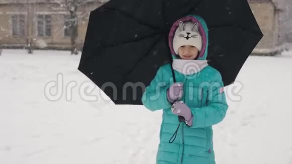 冬天雪下的小女孩在一把黑伞下的学校旁边的街道上视频的预览图