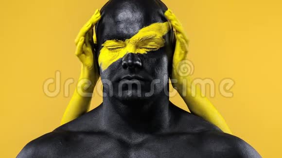 有女性双手的男人健美运动员有黄色的面部艺术和黑色的身体油漆彩色肖像视频的预览图