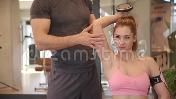 有魅力的女人和一个私人教练在健身房进行哑铃重量训练视频的预览图