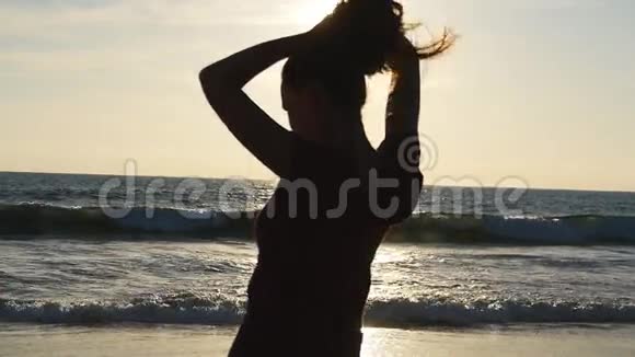 日落时分在海边海滩上扎马尾辫的黑发女郎美丽的女孩在海边挤头发视频的预览图