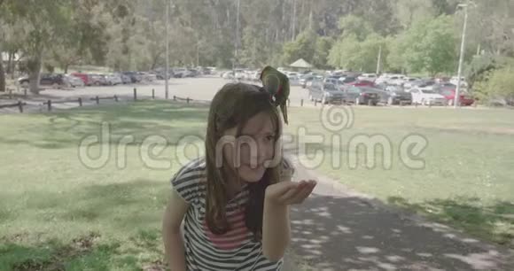 一个年轻的女孩正在用她的手在头上喂一只彩虹鹦鹉当另一只鸟飞到她的头上时视频的预览图
