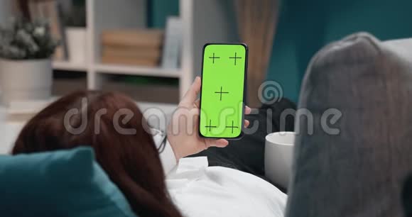 女人在沙发上放松拿着绿色屏幕的电话视频的预览图