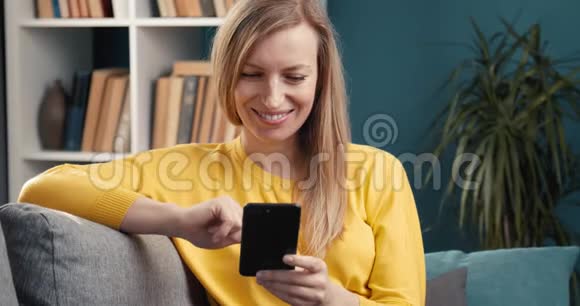 穿黄色毛衣的微笑女人在智能手机上聊天视频的预览图