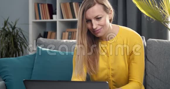 穿黄色毛衣的快乐女人在笔记本电脑上打字视频的预览图