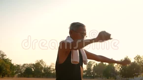 在阳光明媚的日子里亚洲老人在公园锻炼前伸展肌肉保健概念视频的预览图