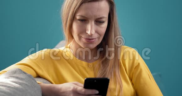 迷人女人在沙发上用智能手机放松的肖像视频的预览图