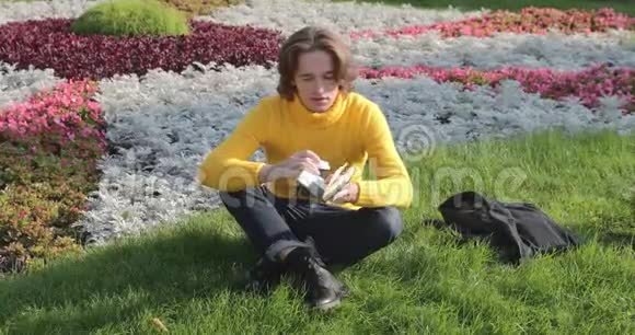 年轻人在公园里喝咖啡看书他微笑着休息一下穿着一件黄色毛衣视频的预览图