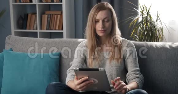 漂亮的女士在沙发上放松时使用平板电脑视频的预览图