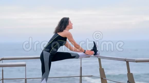 在海滨活动的妇女慢跑者做腿部伸展运动视频的预览图