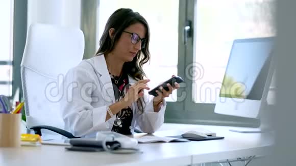 漂亮的年轻女性妇科医生在开始在诊所咨询之前使用她的手机视频的预览图