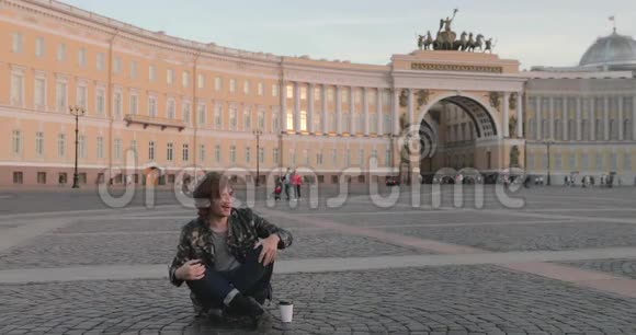 这位美丽的年轻人坐在皇宫广场上日落时分喝咖啡他穿着一件军服视频的预览图