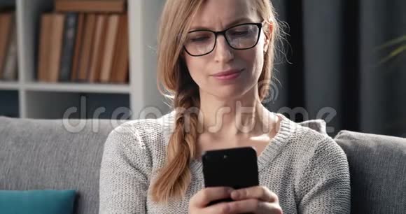 快乐的女人坐在沙发上在智能手机上发短信视频的预览图