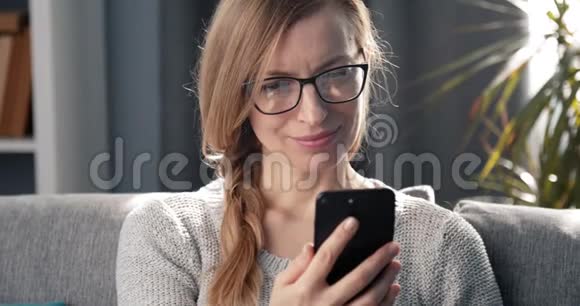 微笑的女人在沙发上放松时使用智能手机视频的预览图