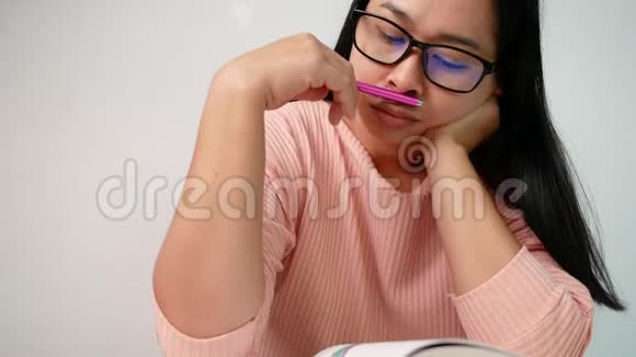 亚洲年轻的女人拿着笔在她的手中一边读着一本书带着深思熟虑坐在家里的客厅里选择性泡沫视频的预览图