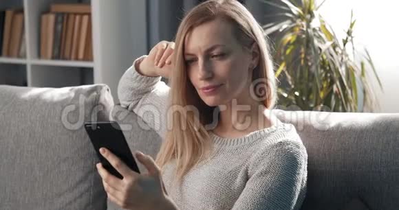 在空闲时间微笑的女人使用智能手机视频的预览图