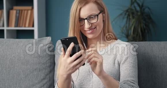 戴耳机的女人在沙发上放松使用智能手机视频的预览图