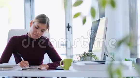 集中精力的年轻商务女性在办公室做笔记时在手机上接收信息视频的预览图