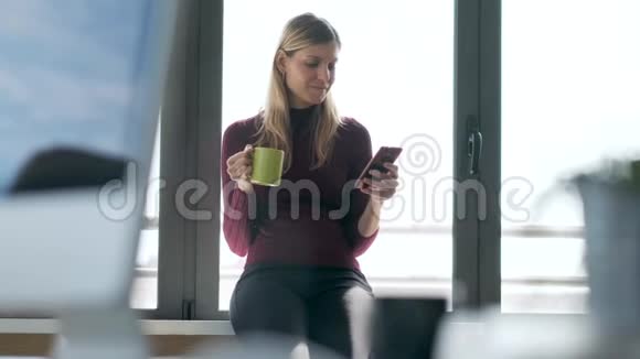 漂亮的年轻商务女性在办公室喝咖啡时用手机发信息视频的预览图