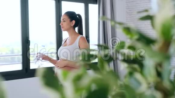 漂亮的年轻孕妇站在家里喝水视频的预览图