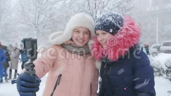 两个十几岁的女孩在一场降雪期间拍摄了一部vlog女朋友的博客们正在报道这座城市的一座雪丘视频的预览图